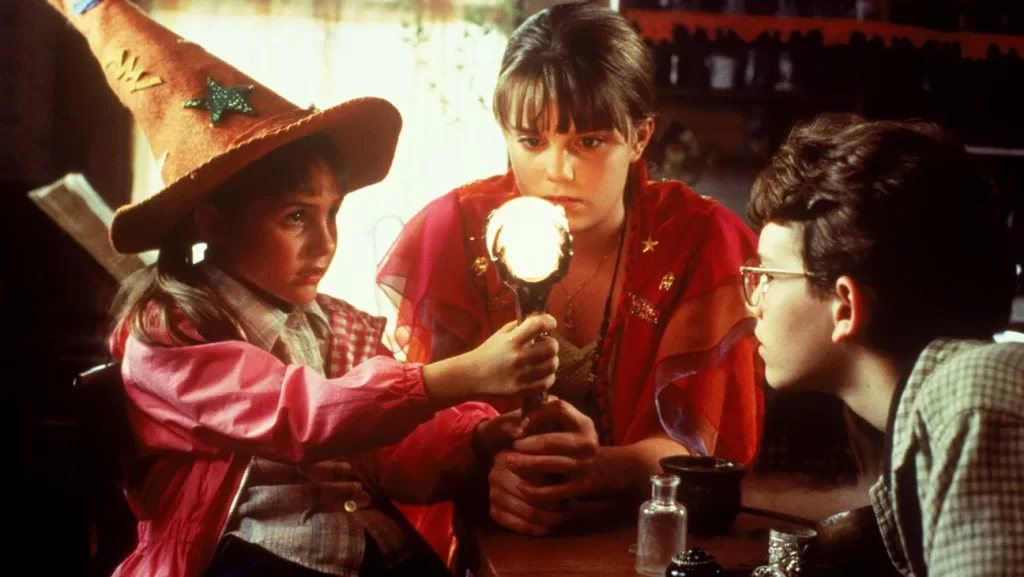 3 kids are staring at a glowing wand and the two girls are holding the wand. HalloweenTown The Best Halloween Movies To Watch During October 