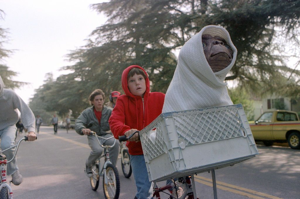 Kids riding down the rode on bikes and one is carrying E.T.